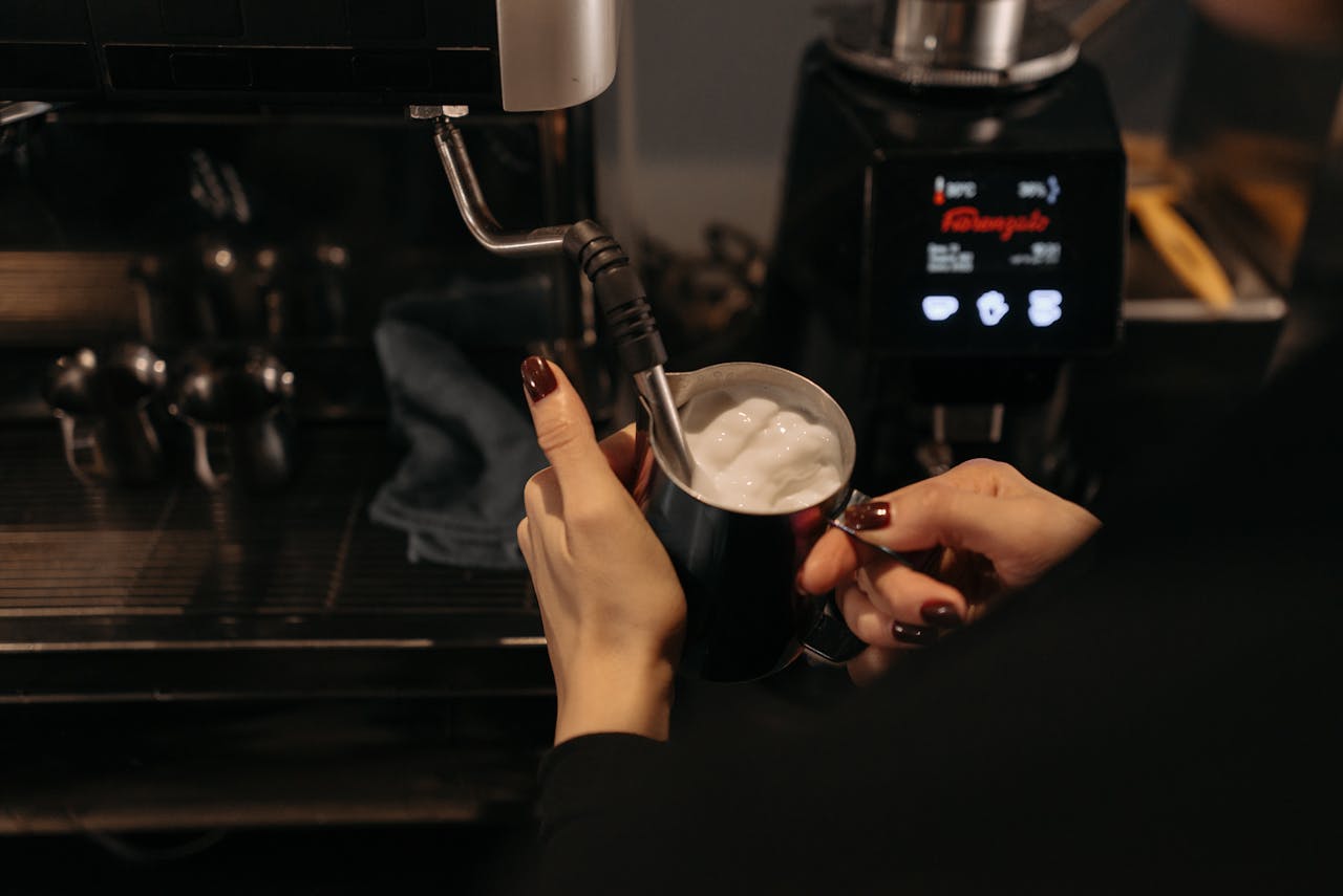 A barista uses a steam wand to froth milk in a café, focusing on coffee preparation.